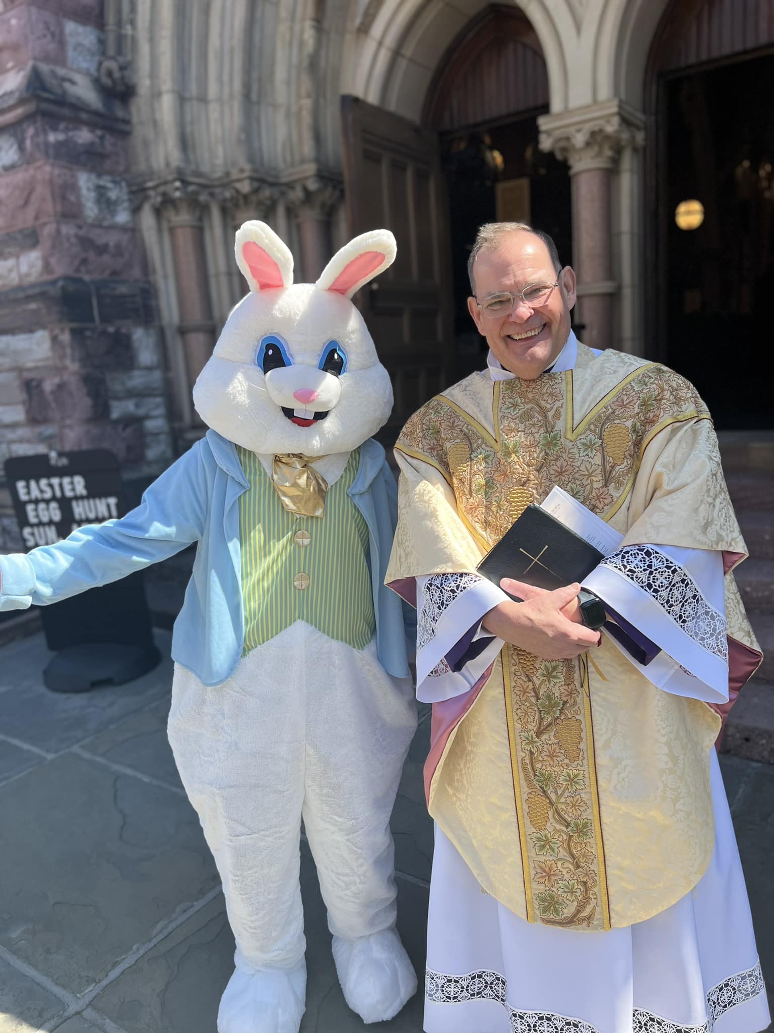 priest in gold and white vestments standing next to easter bunny